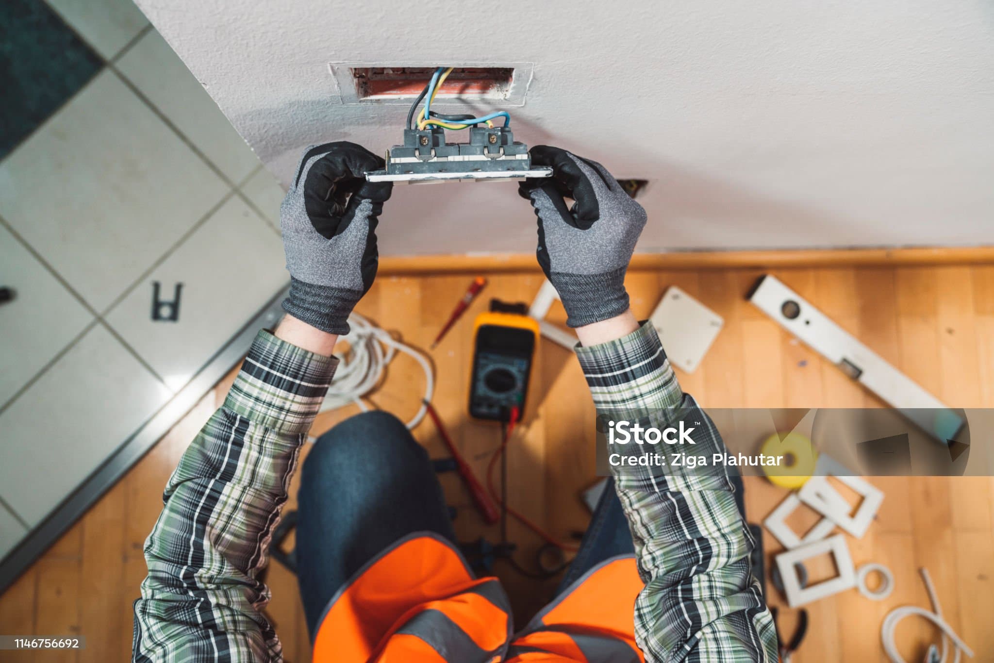 Overhead view of an electrician’s gloved hands fitting a wall socket, tools laid out on the floor below