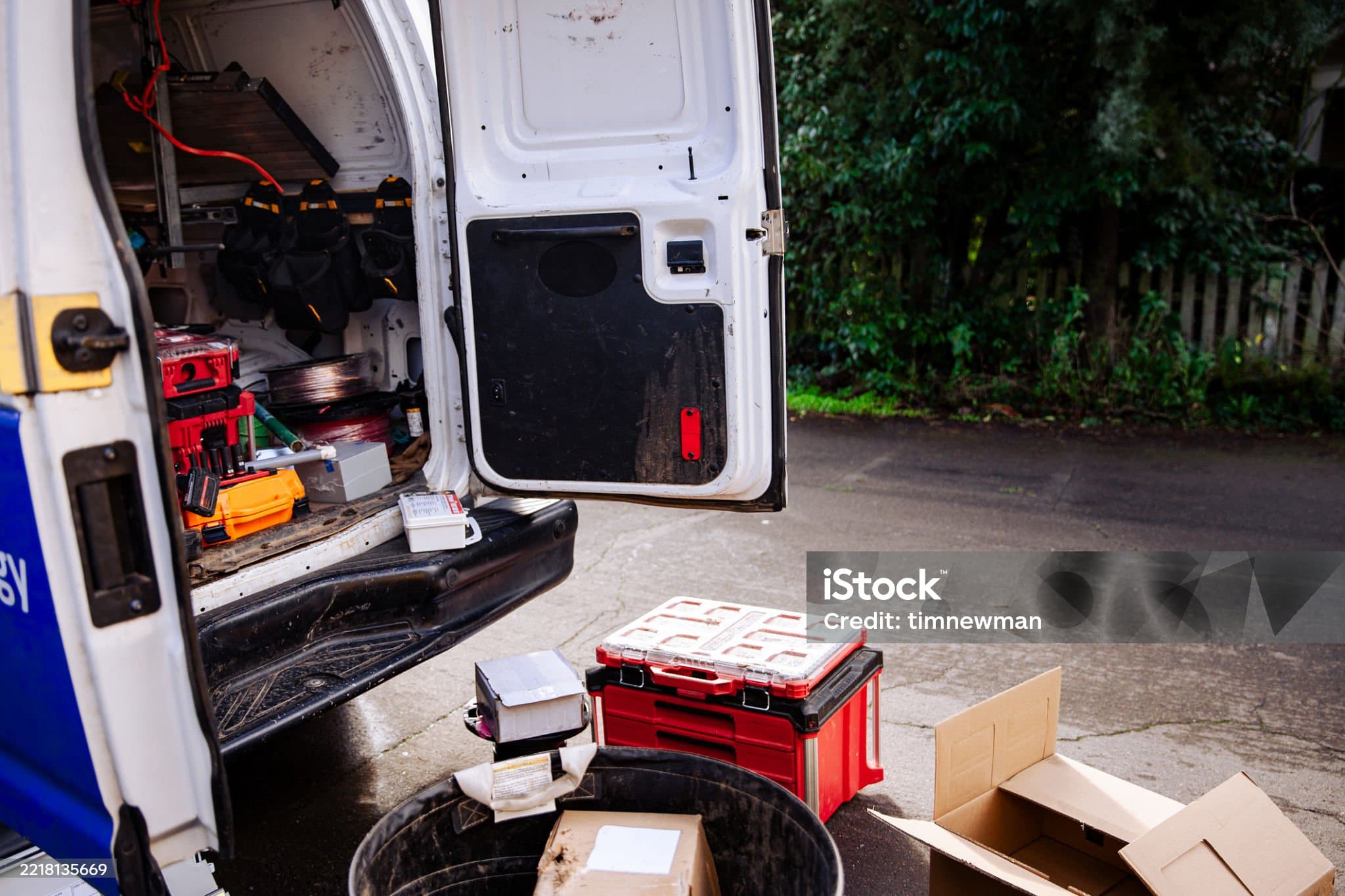 The open rear doors of a working electrician’s van on a driveway, tools and cable drums inside