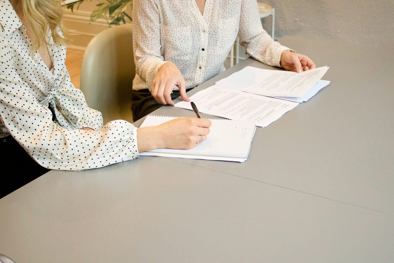 A woman signing paperwork while another person points at the documents