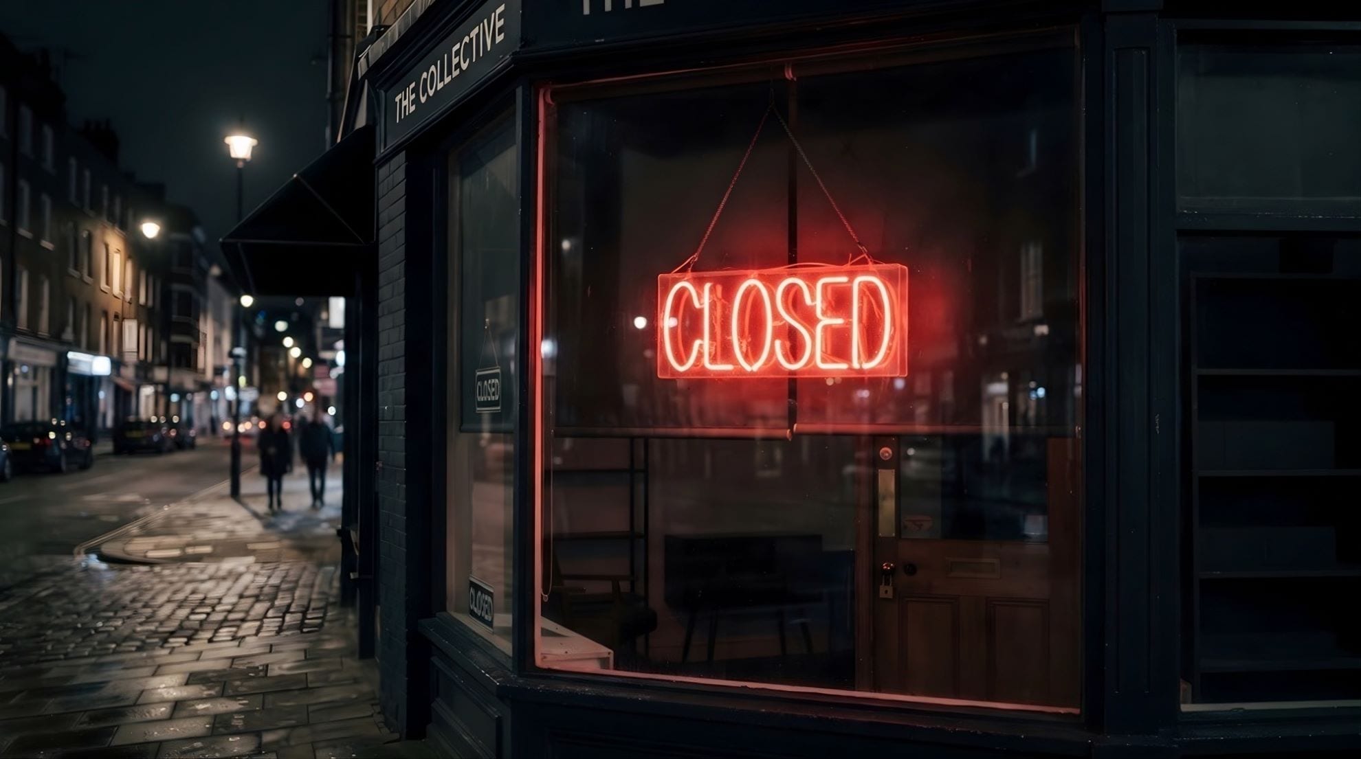 A lit but empty shop interior seen from the street at night, a figure passing outside