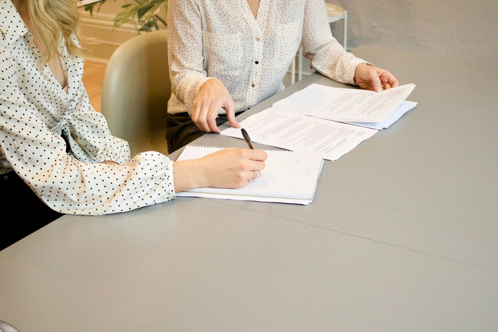 A woman signing paperwork while another person points at the documents