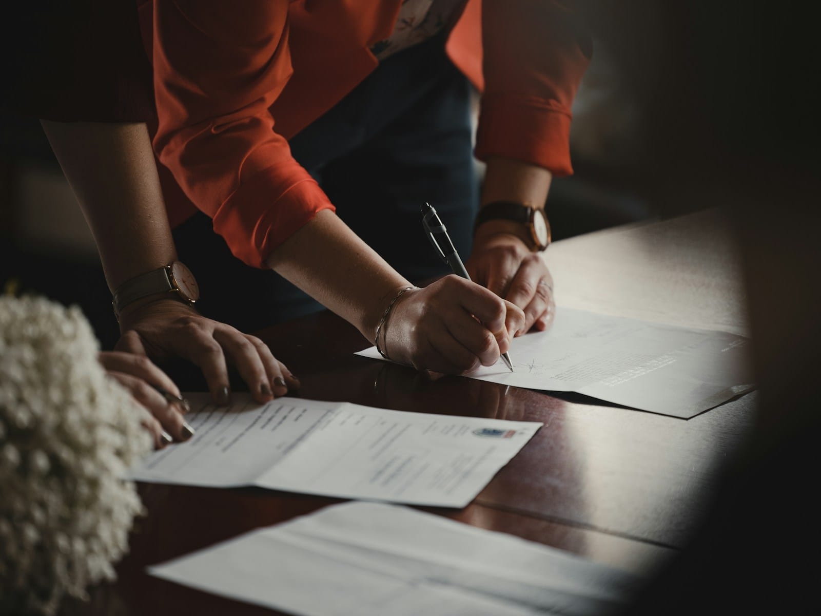 A person in an orange shirt writing on a white document